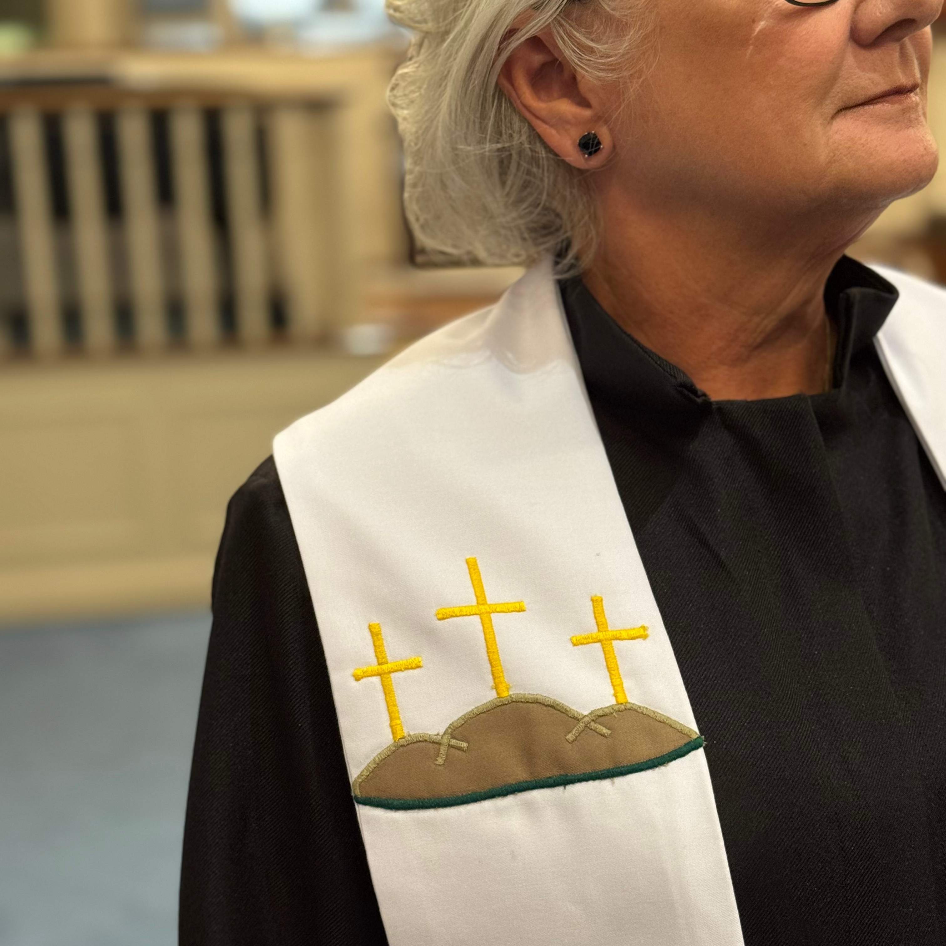 Person wearing a black robe with a white stole featuring embroidered crosses and a hill.