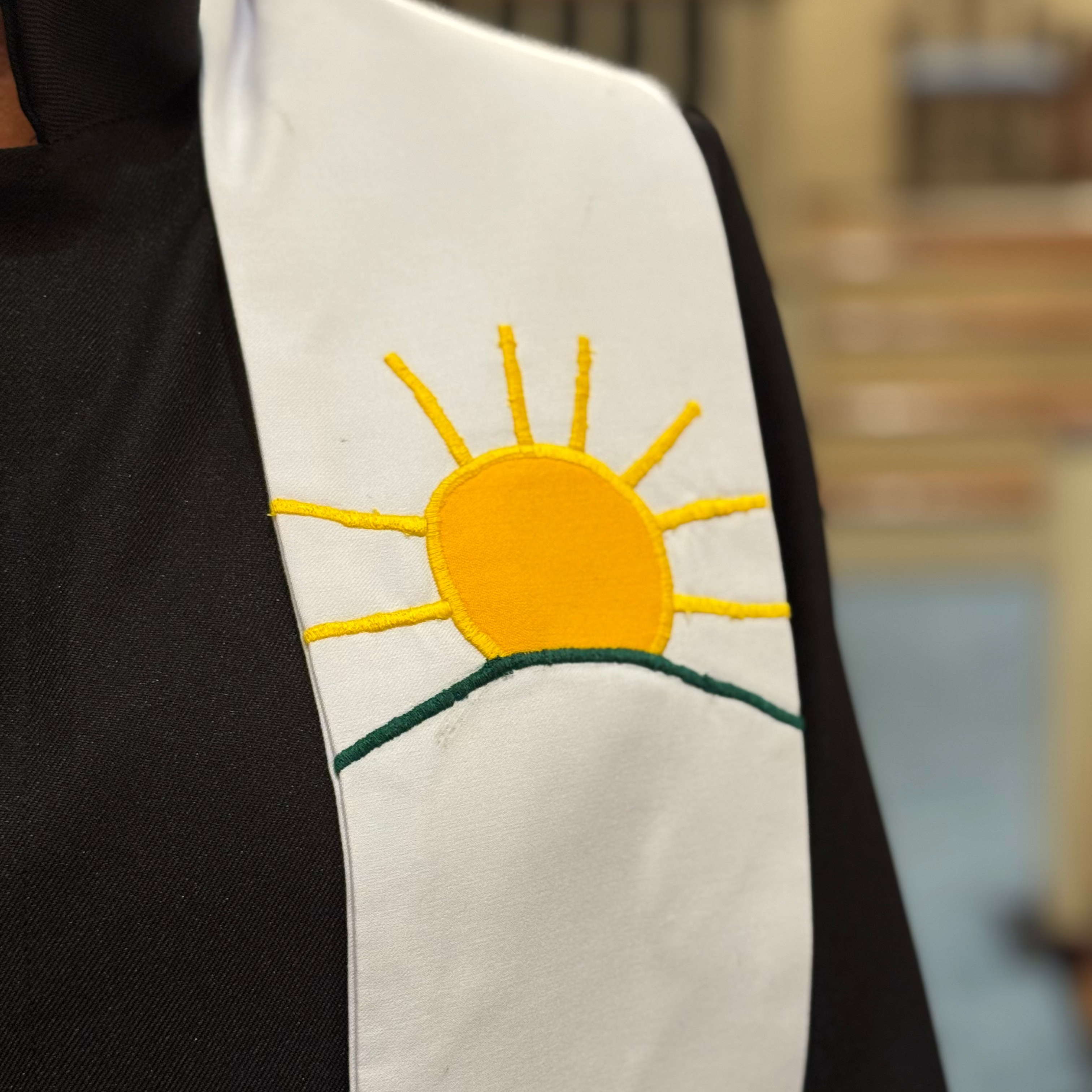 White stole with a yellow sun design worn by a person, blurred background