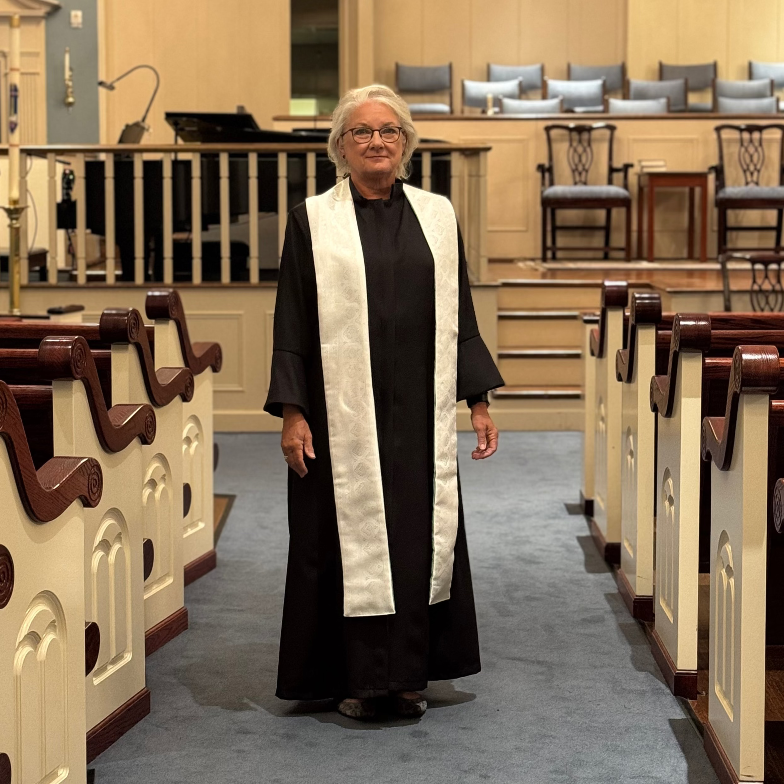 Person in a black robe with a white stole standing in a church nave.