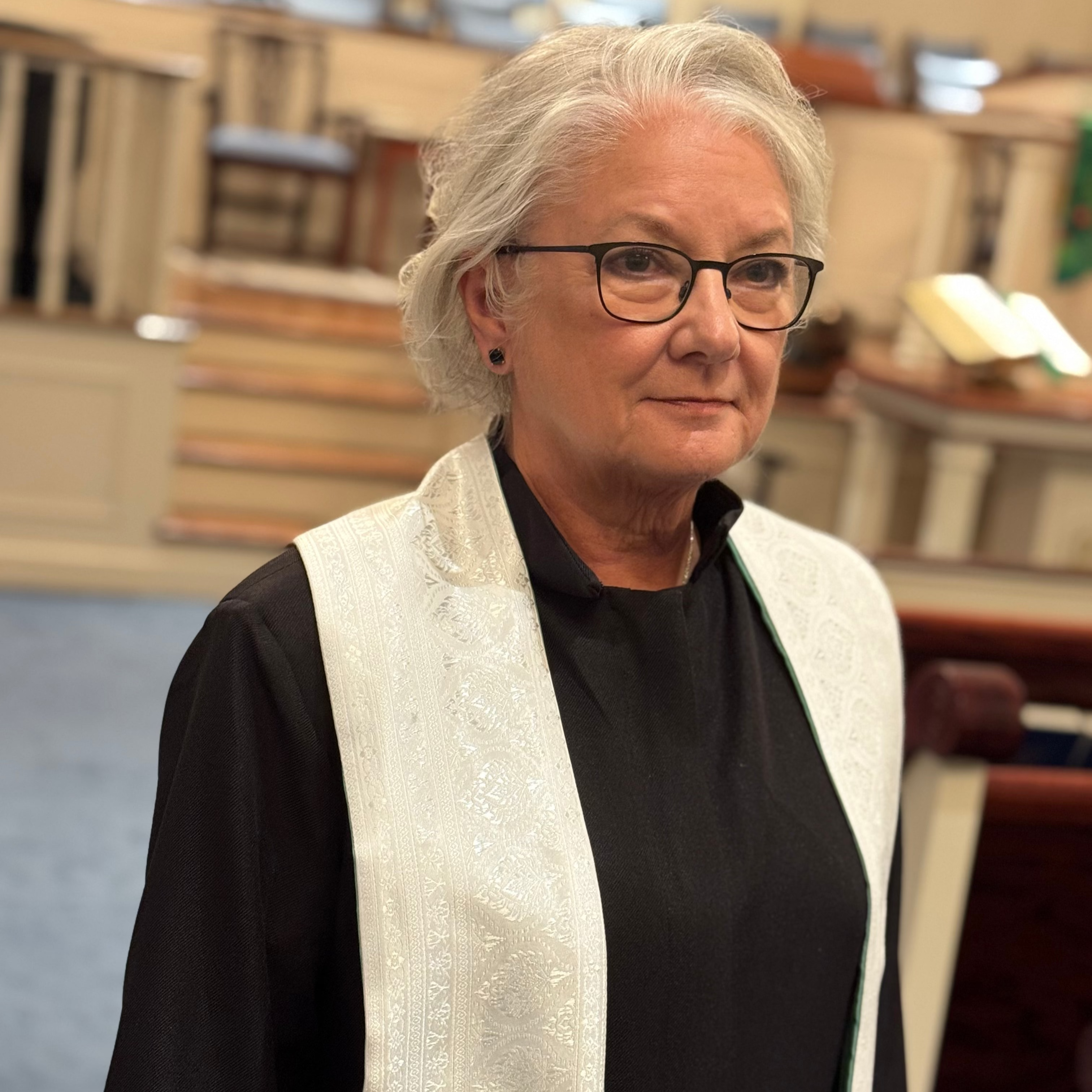Woman wearing glasses and a white vest over a black outfit in an indoor setting