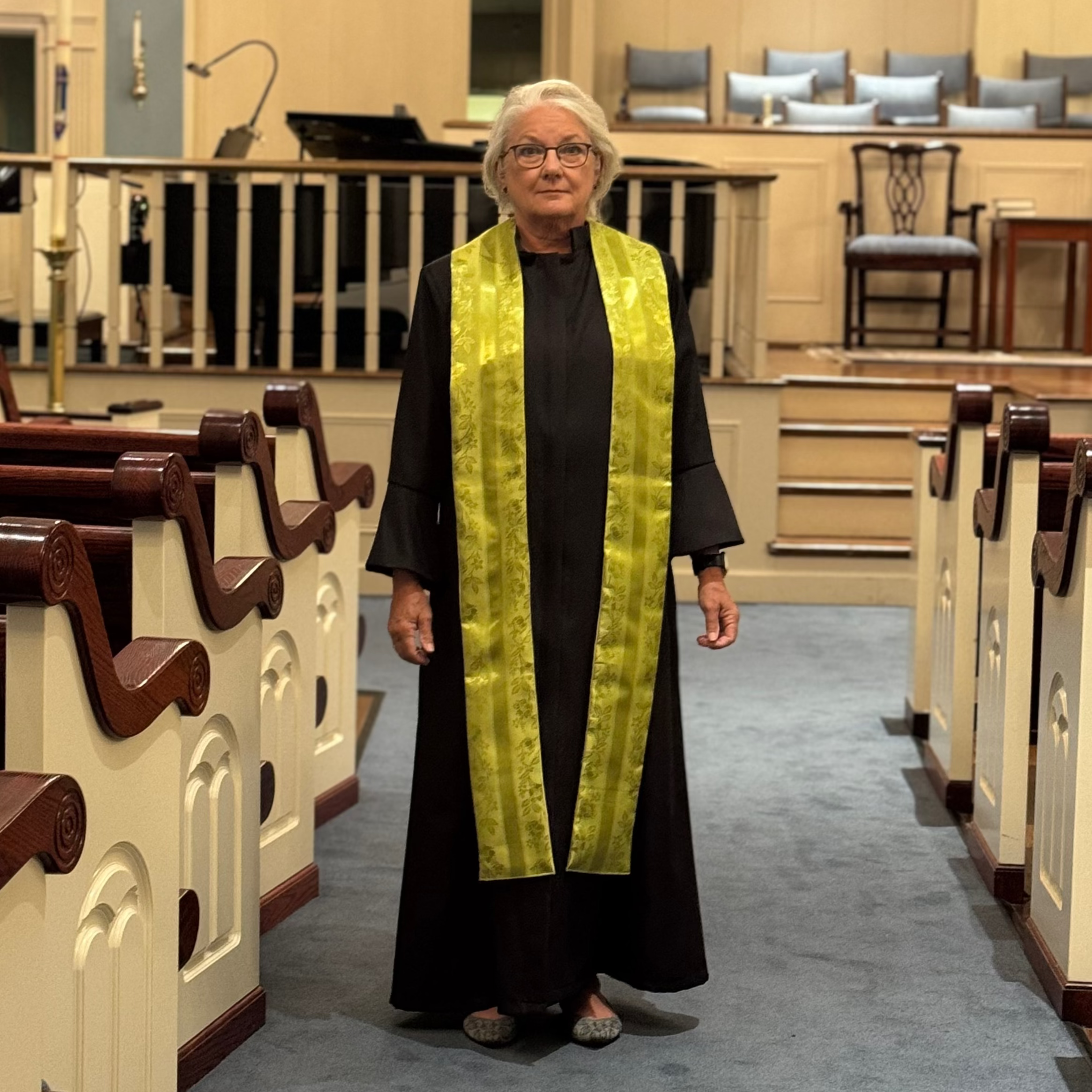 Person in a church setting wearing a black robe and yellow stole.