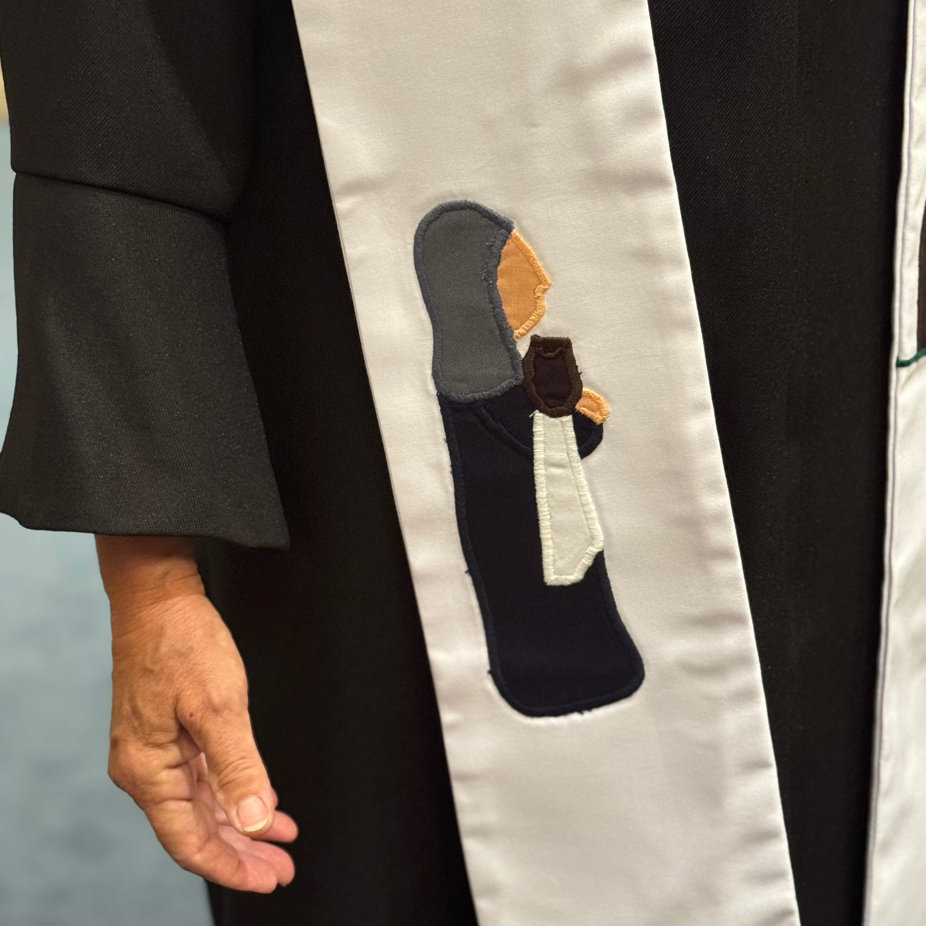Graduation gown with a decorative sash featuring an embroidered design.